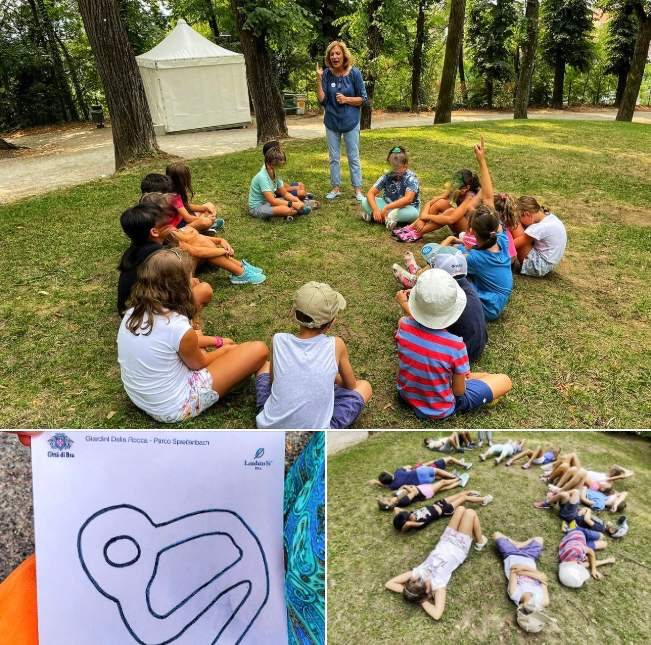 Bambini seduti in cerchio sul prato del parco Belvedere con una volontaria della Comunità