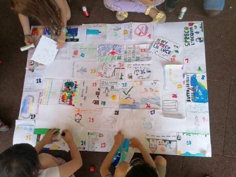 Bambini che disegnano le caselle del Gioco dell’Oca ecologico su un grande cartellone